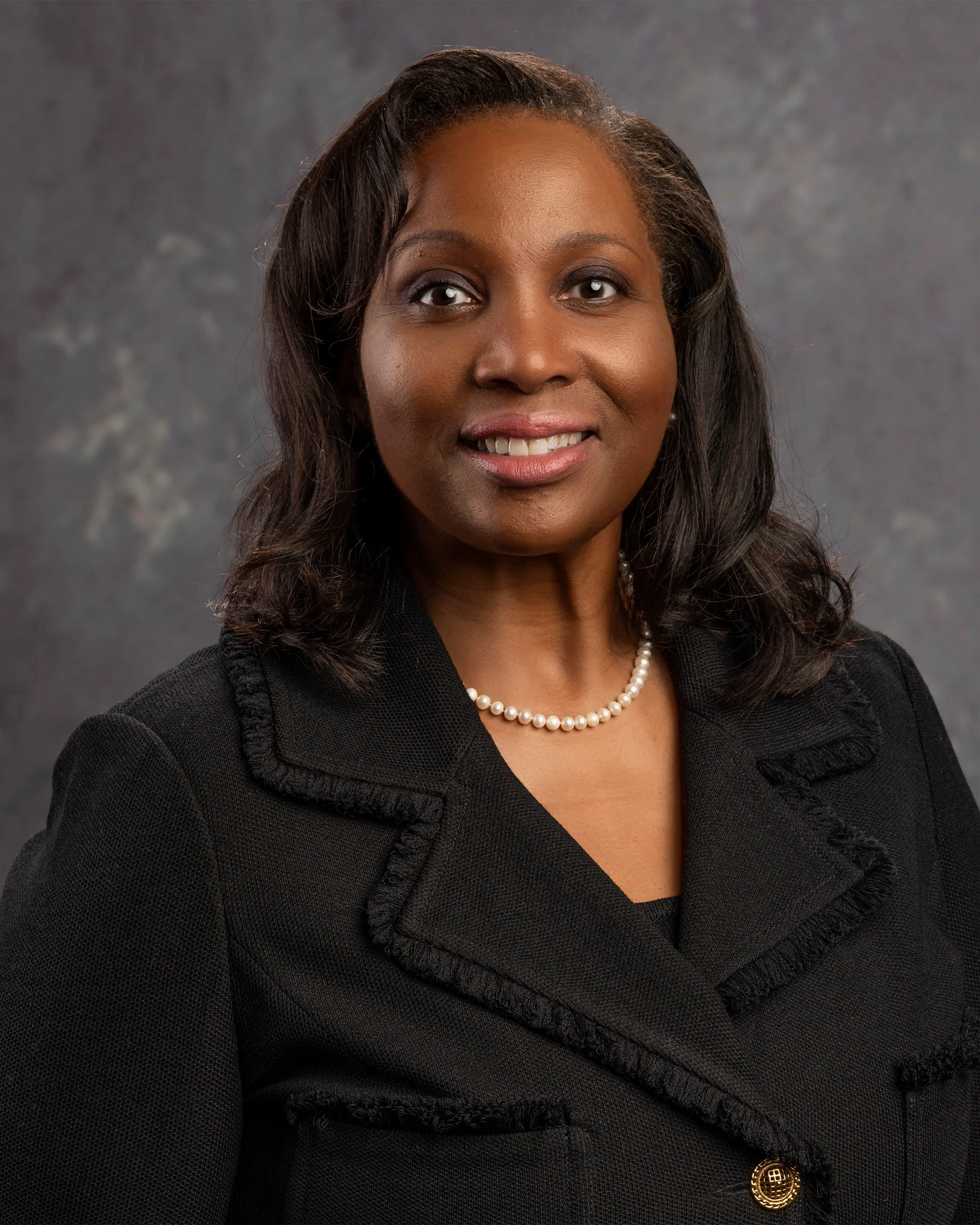 Official portrait of Federal Reserve Governor Lisa D. Cook seated in a dark blazer with the American flag behind her.